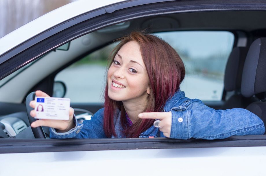 Een vrouw lacht in een auto, houdt een kopje vast en wijst ernaar, met sneeuw buiten het raam.
