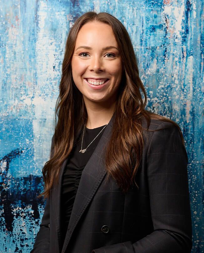 Smiling woman in a black blazer against a blue textured backdrop