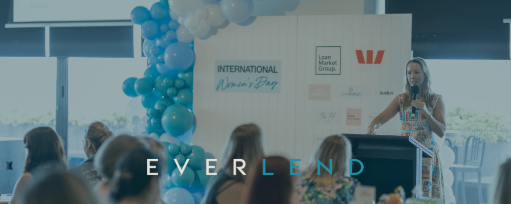 People seated at a blue-lit event stage with speakers and balloon decor, “EVERLAND” displayed on screen