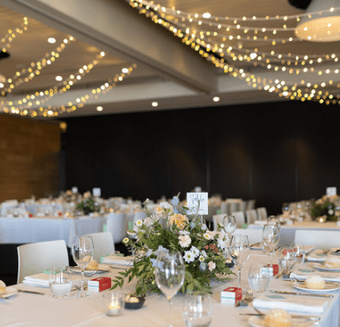 Elegant banquet hall with candlelit round tables, floral centerpieces, and warm string lights overhead