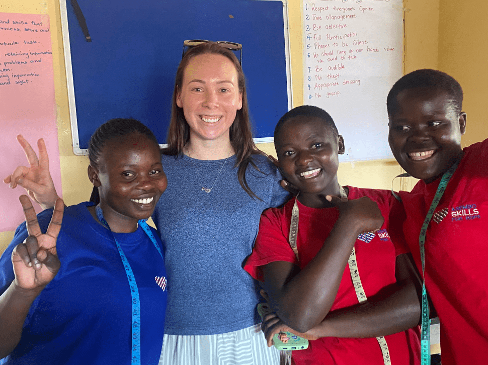Four smiling people pose in a classroom, one holding up a peace sign.