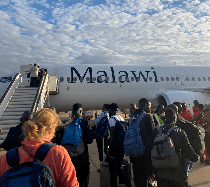 Travelers board a Malawi Airlines plane on the tarmac under a cloudy sky.