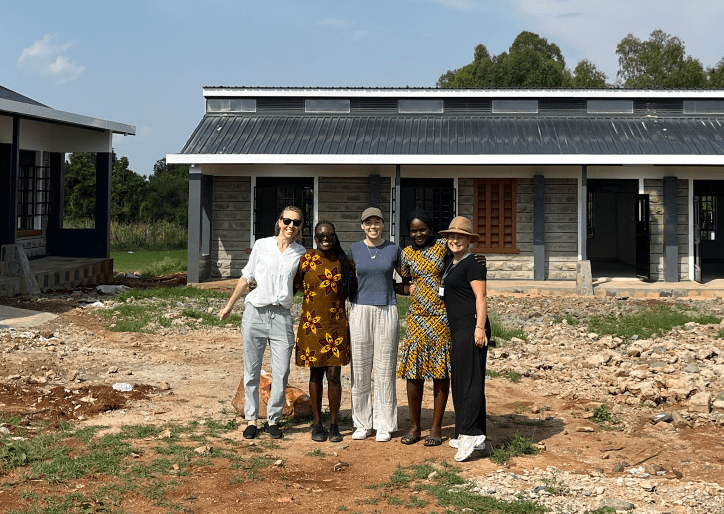 Four people posing in front of a new house under construction on a sunny day