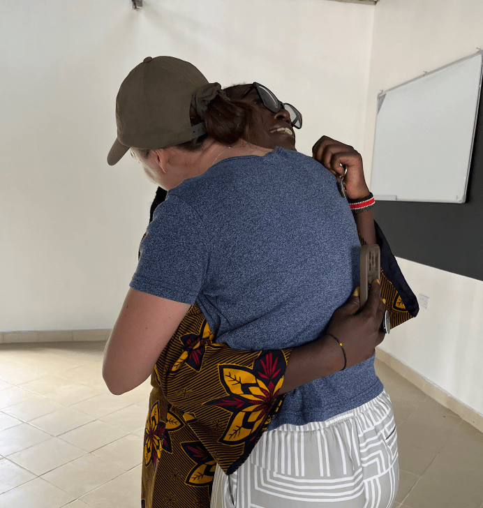 Two people hugging indoors, one in a blue shirt and cap, the other in patterned clothing.