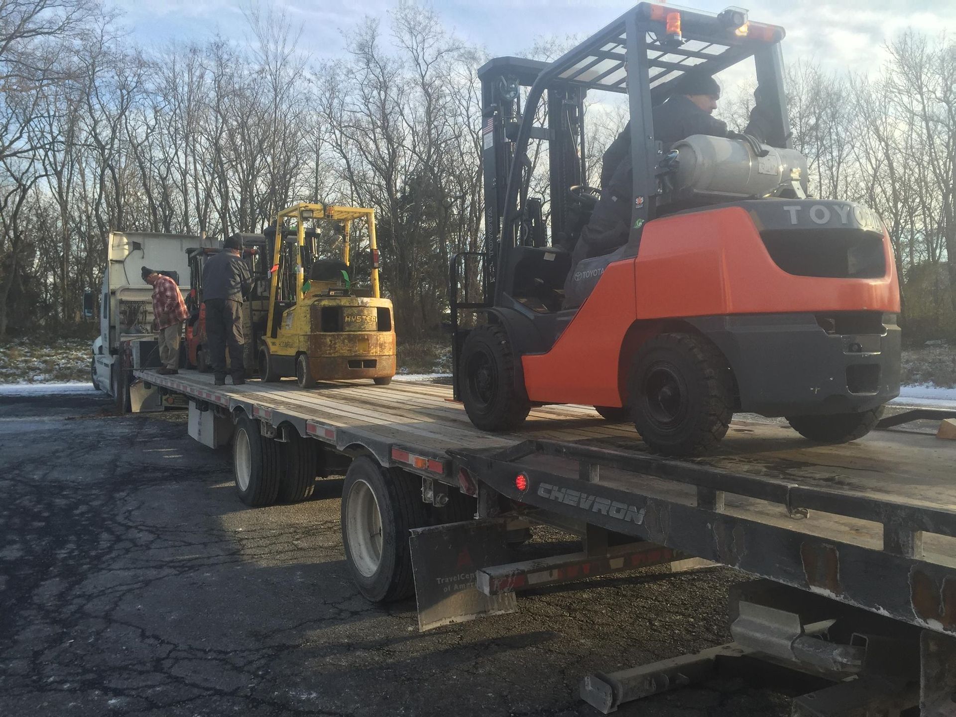 A man is driving a forklift on top of a flatbed truck.