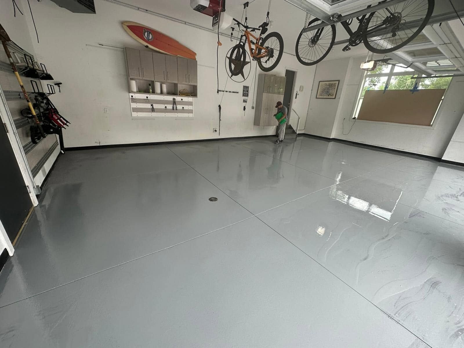 Bright garage interior with polished gray floor, hanging bicycles, wall shelves, and a person near the back wall