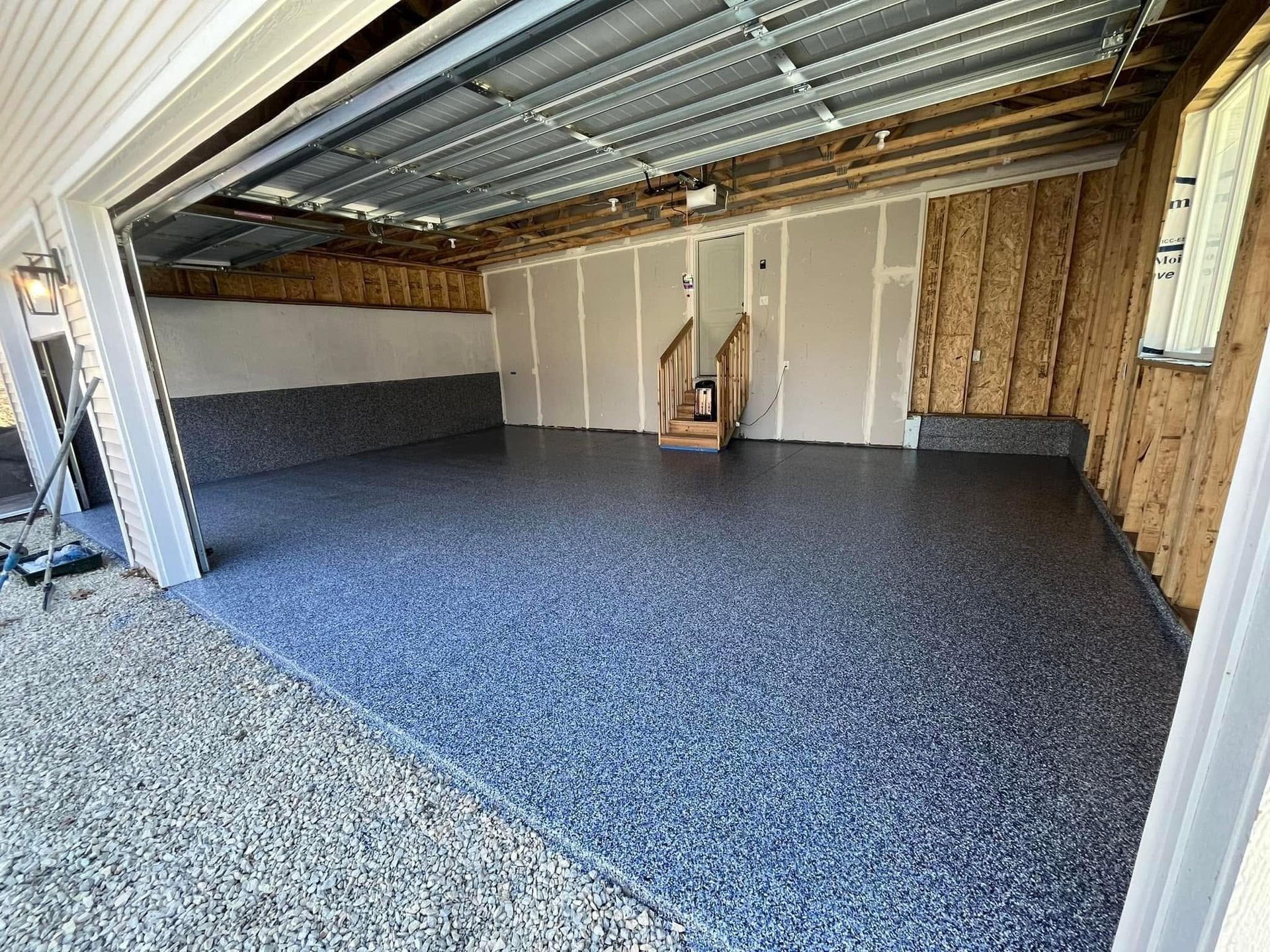 Empty garage with gray speckled floor, exposed roof beams, and a small ladder against the back wall