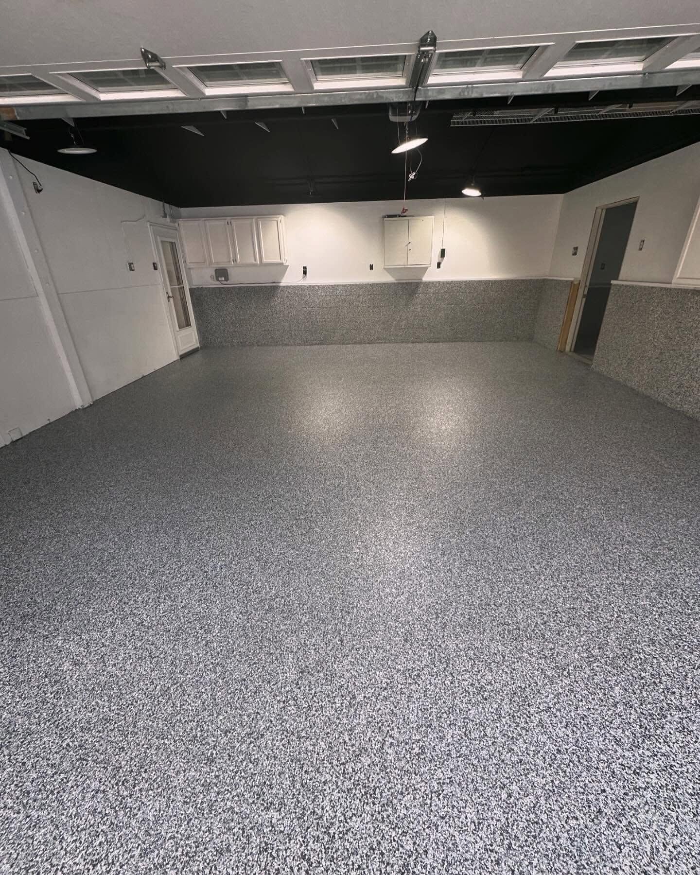 Empty garage with gray speckled floor, white walls, and overhead lights.