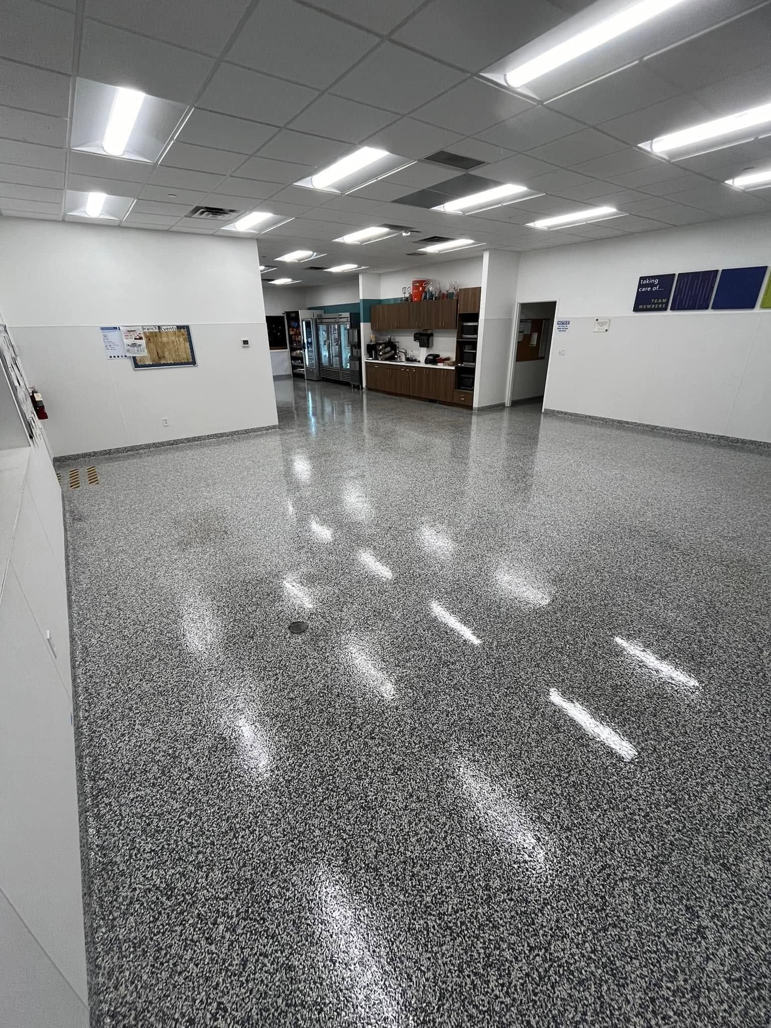 Empty indoor lobby with speckled floor, white walls, fluorescent lights, and a doorway in the back