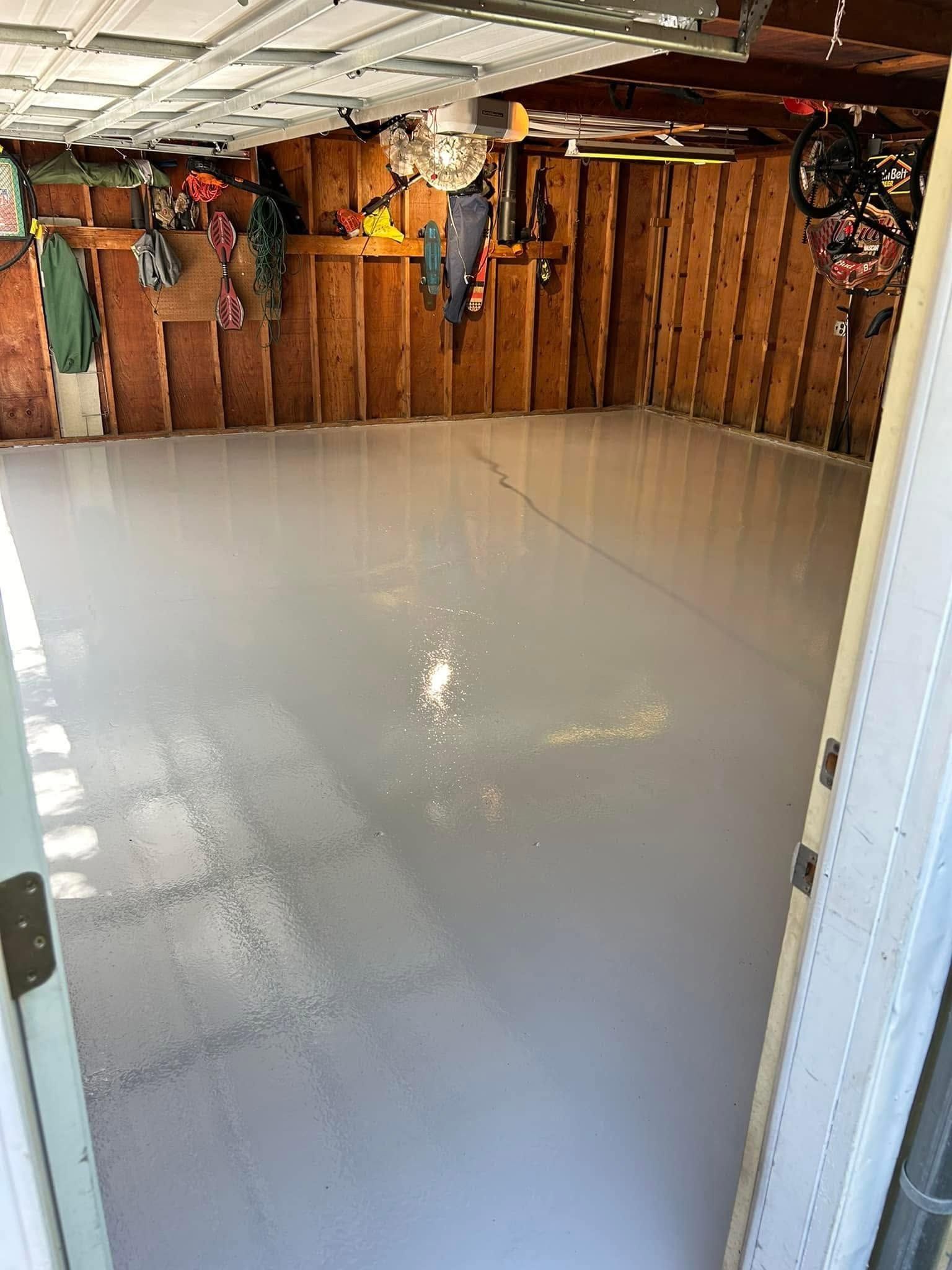 Empty garage with glossy gray epoxy floor and exposed wooden walls, viewed from the doorway