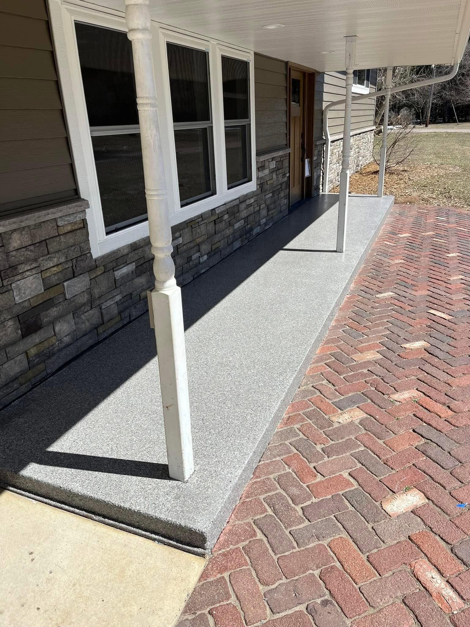 Brick house porch with white posts, windows, and a red herringbone walkway beside a gravel strip.
