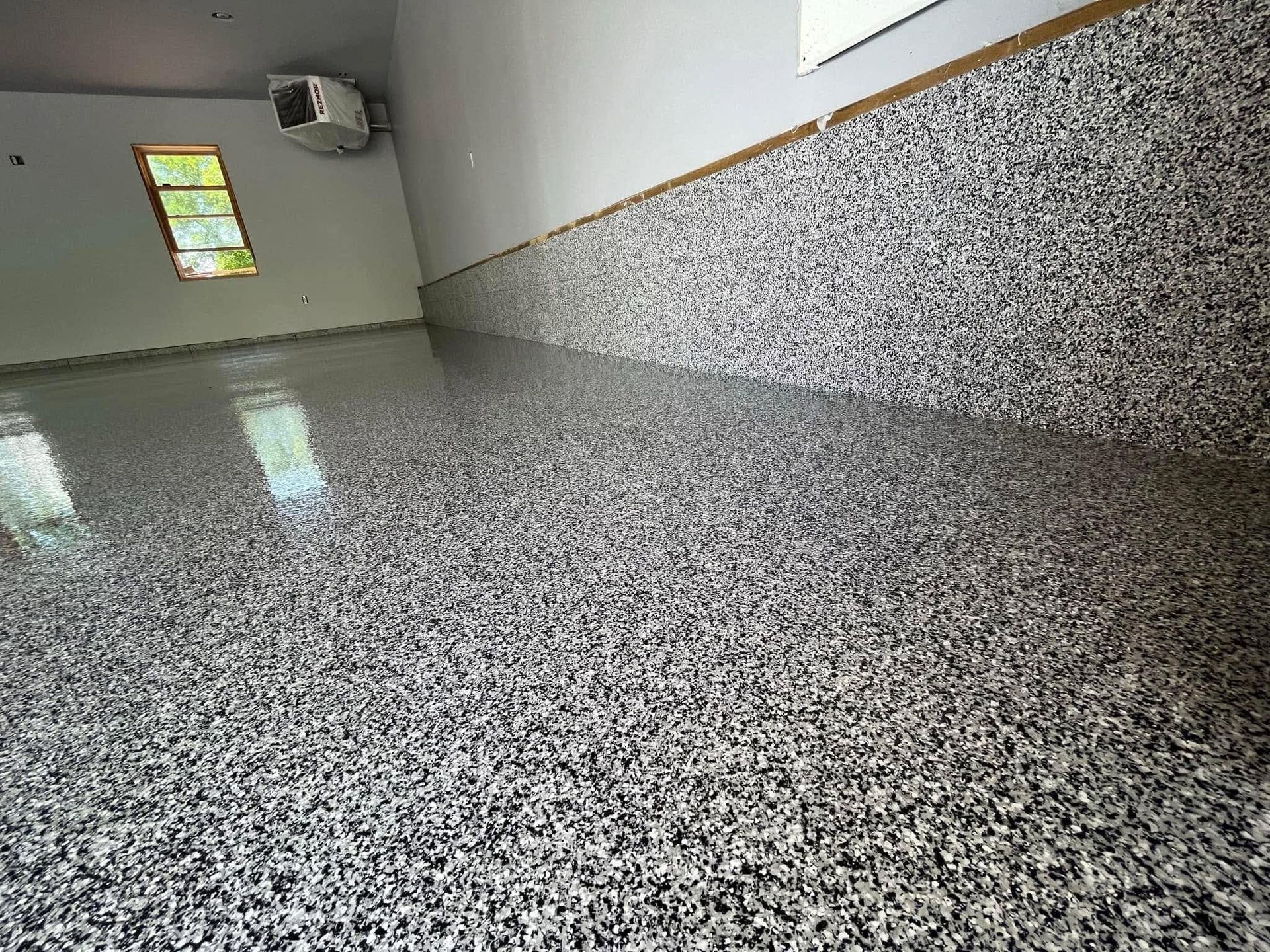 Empty room with speckled gray floor, white walls, and a small window near the ceiling.