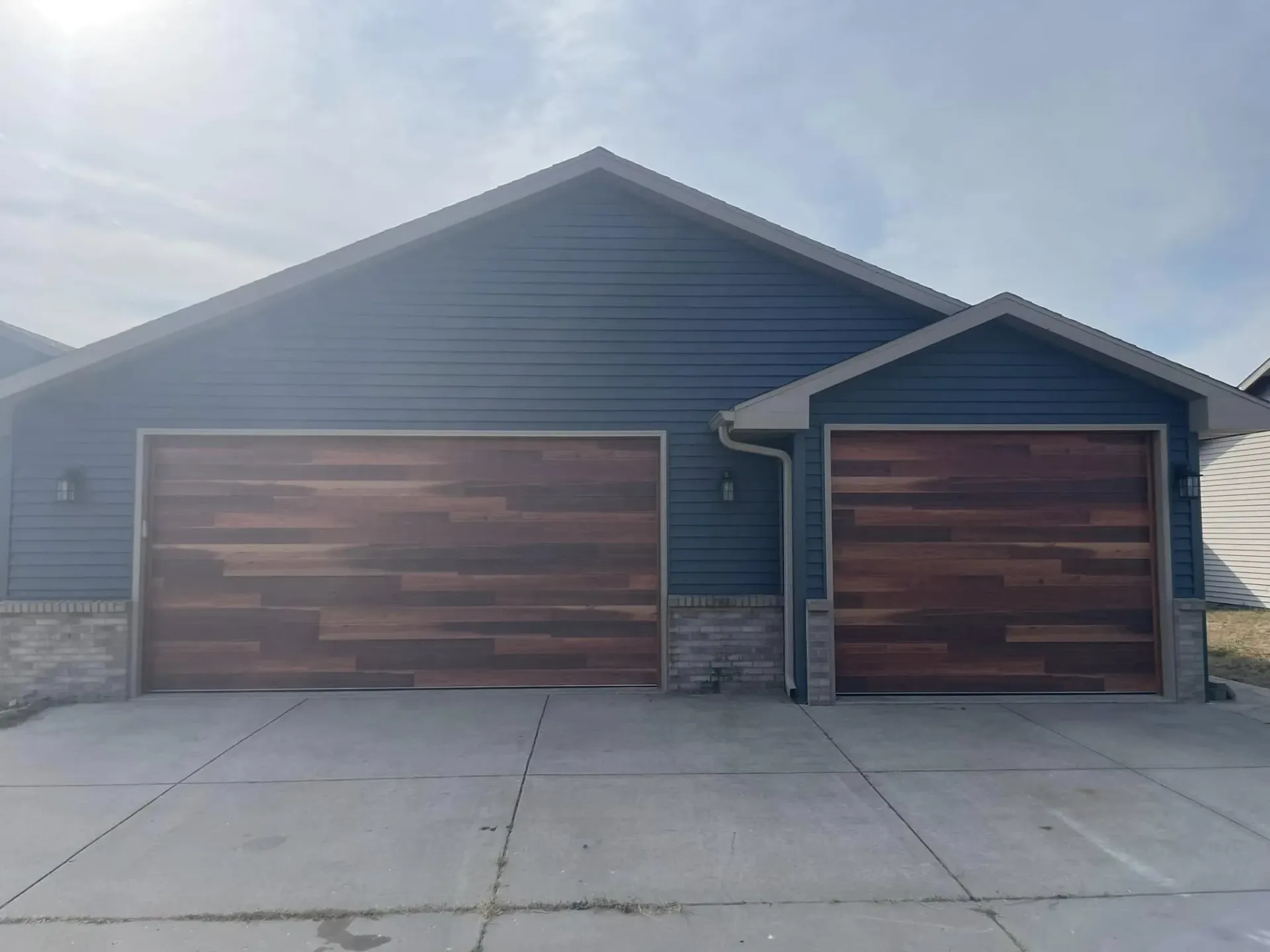 Wood-look double and single garage doors installed on a blue house in South Beloit, IL for a dramatic curb appeal upgrade.