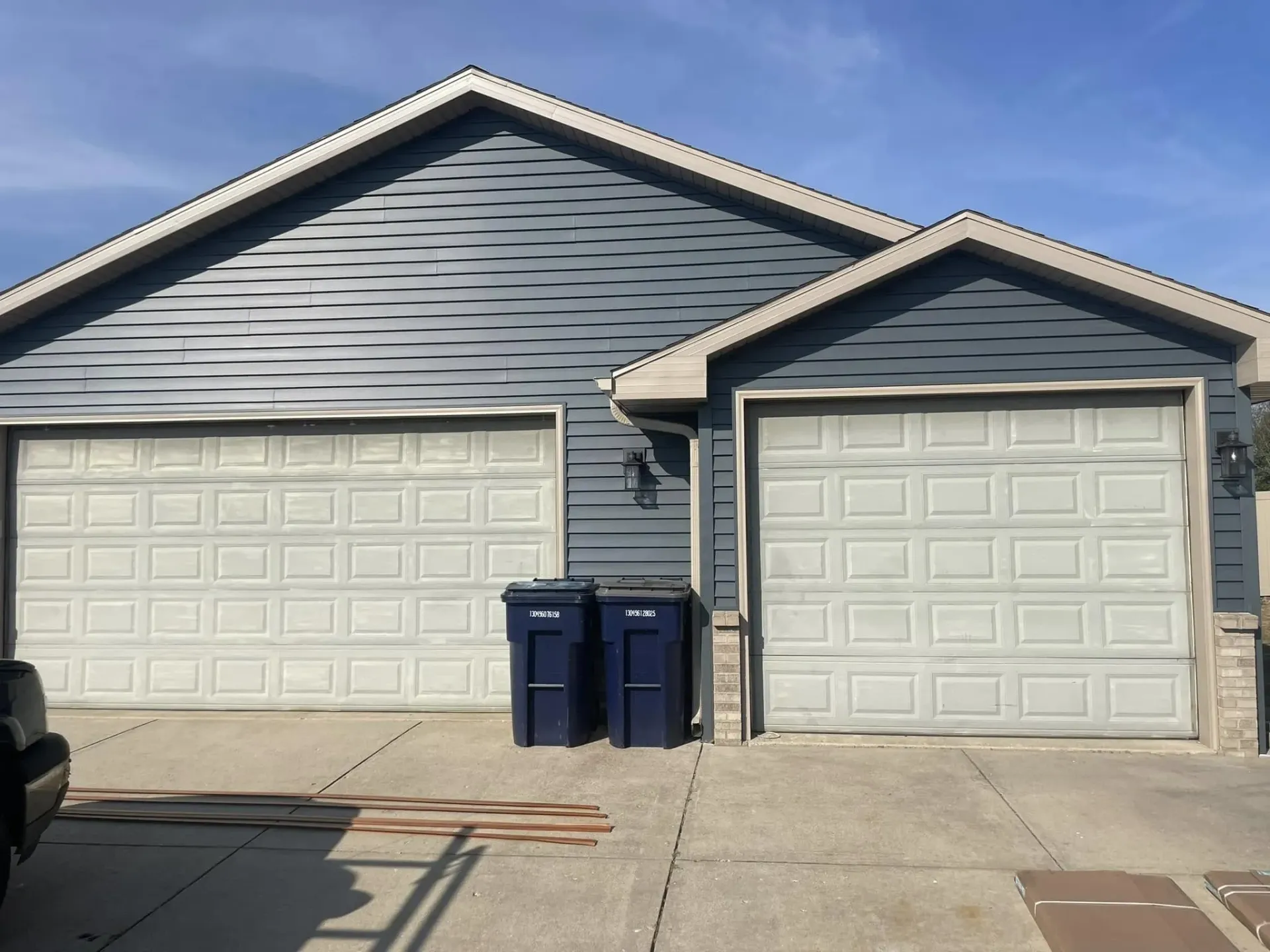 White raised-panel double and single garage doors on a blue house before a garage door replacement in South Beloit, IL.
