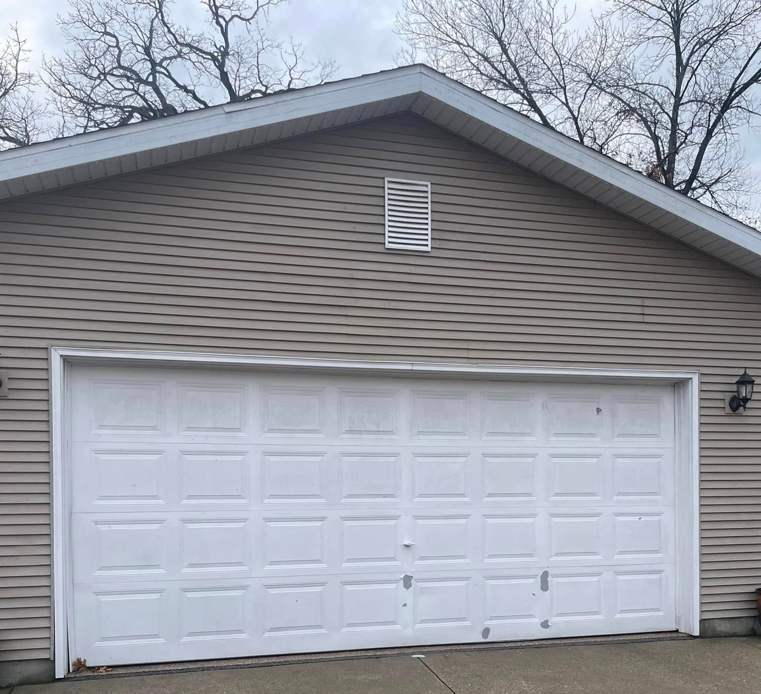 White double garage door on a beige house with gray roof and bare trees in the background