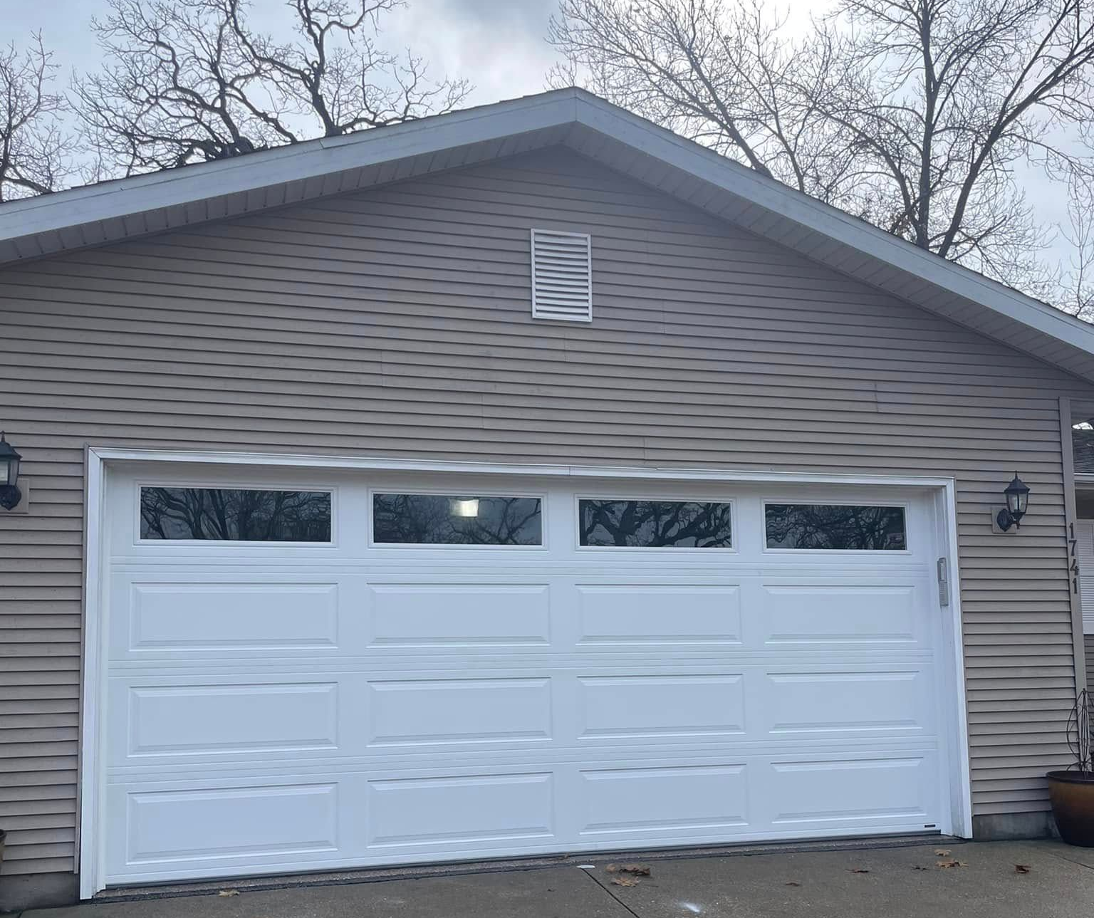 White garage door on a tan house with a gabled roof and small window above it.