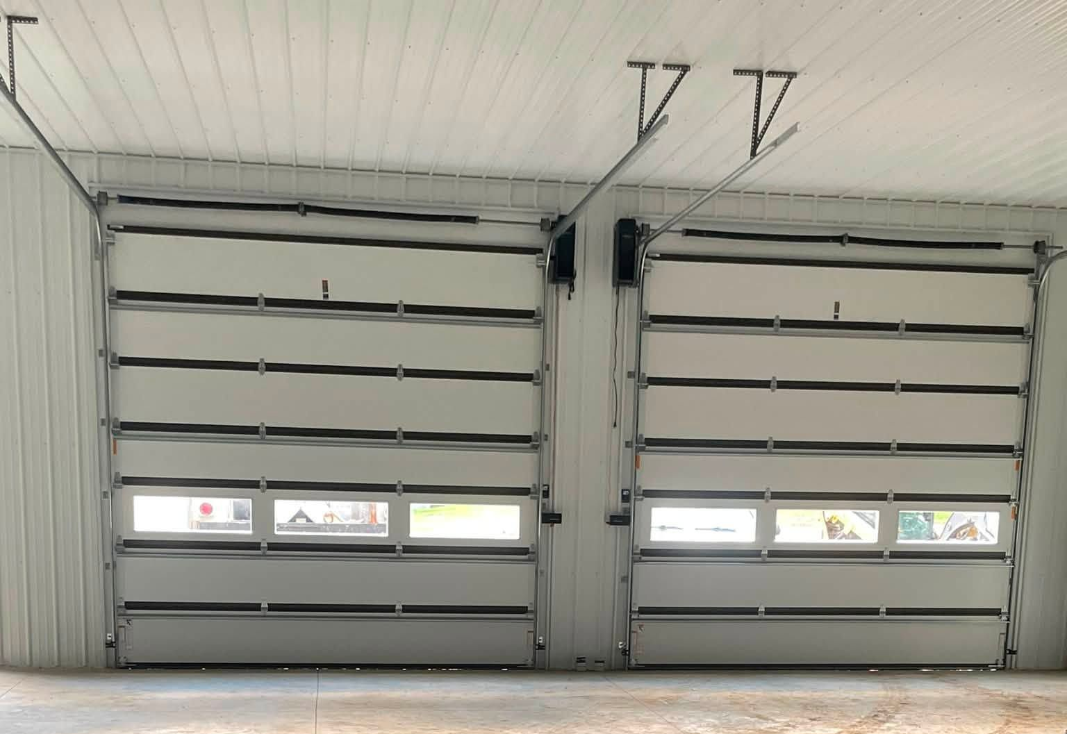 Two insulated garage doors with horizontal windows and new openers installed inside a metal building