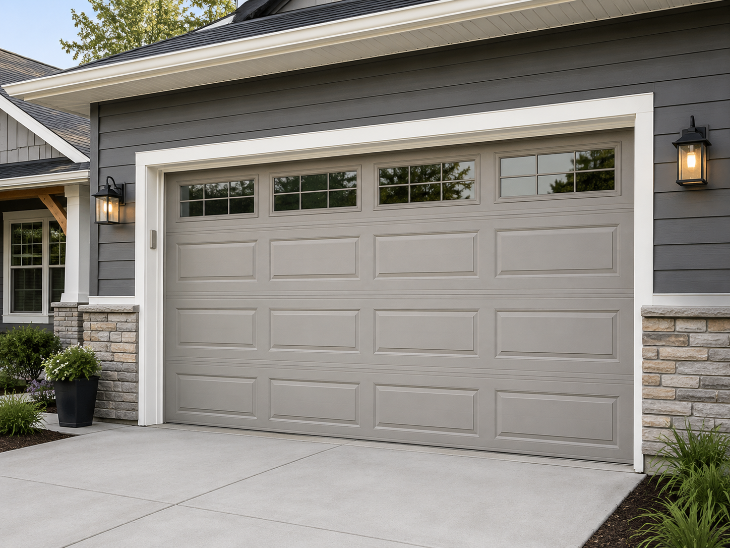 Beige two-car garage door on a gray house exterior with stone accents and wall lanterns