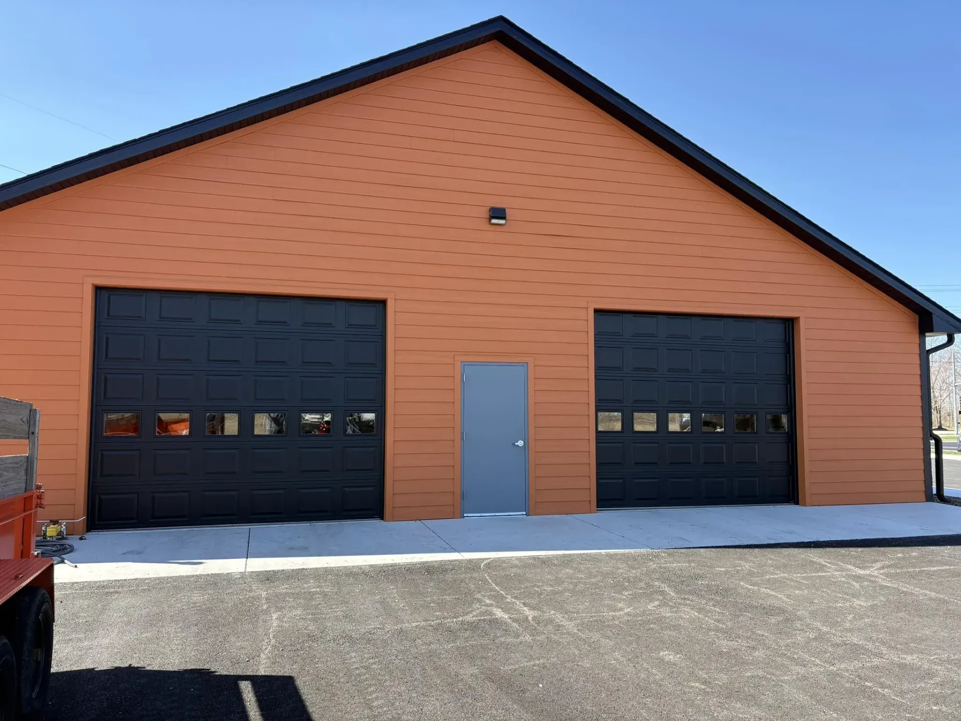 Black garage doors with windows installed on an orange detached garage building