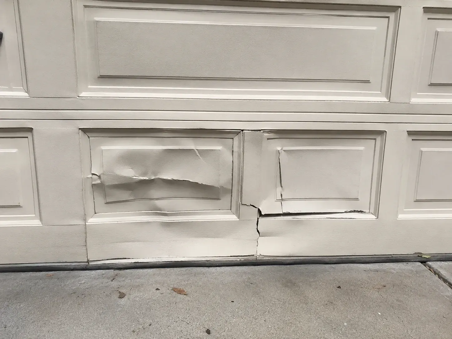 Damaged garage door panels with dents and cracks needing residential repair