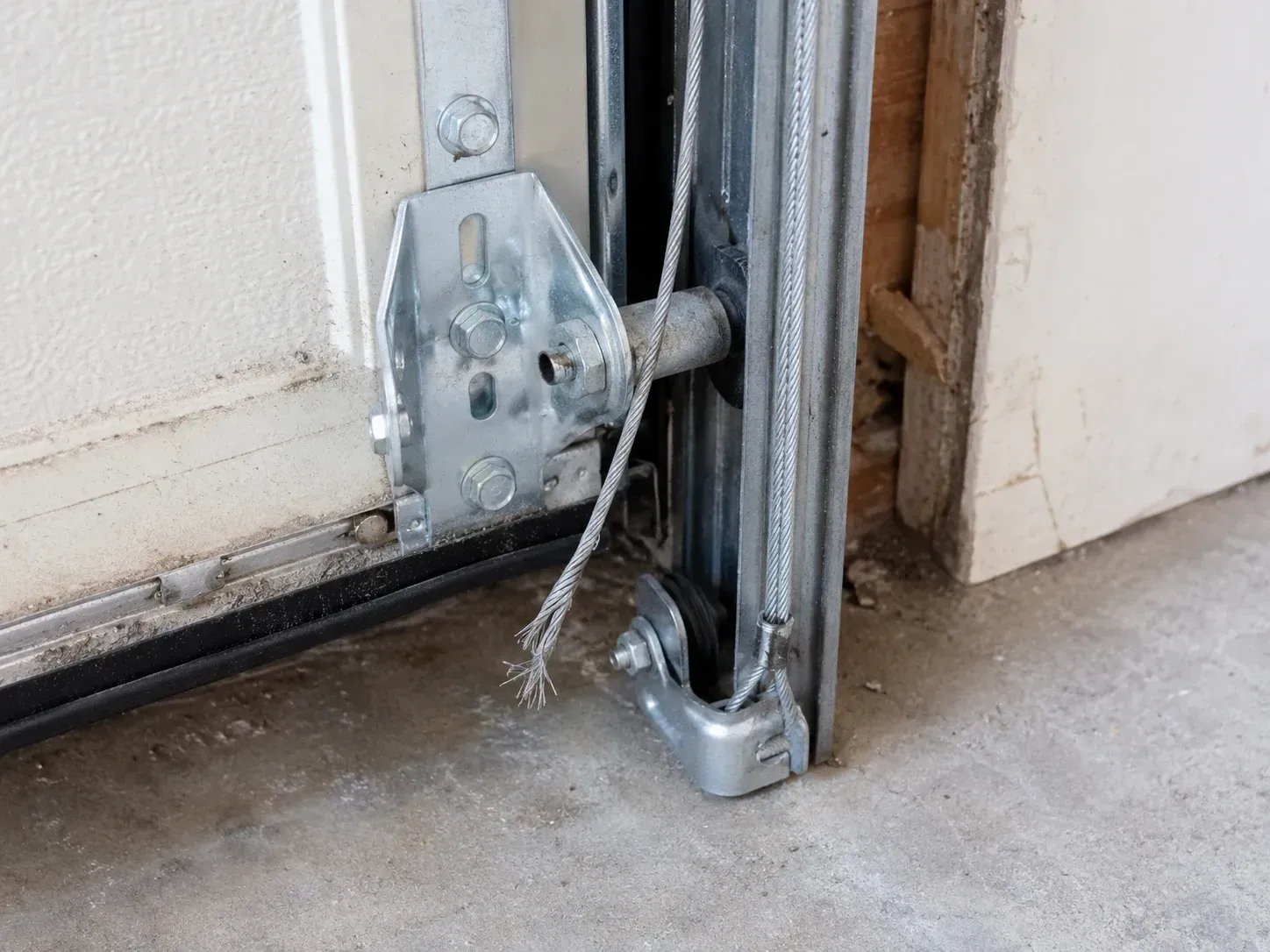 Frayed garage door cable needing repair near the bottom bracket and track