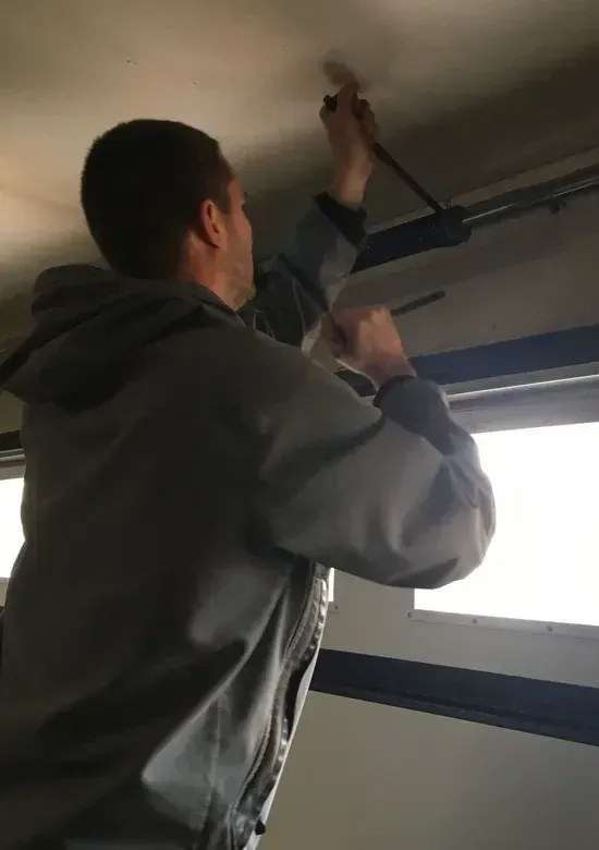 Garage door installation technician adjusting overhead door hardware in Roscoe IL