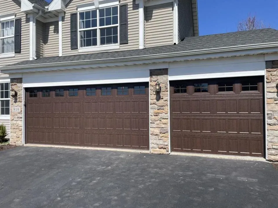 Brown wood-look garage doors with windows on a stone-accent residential home