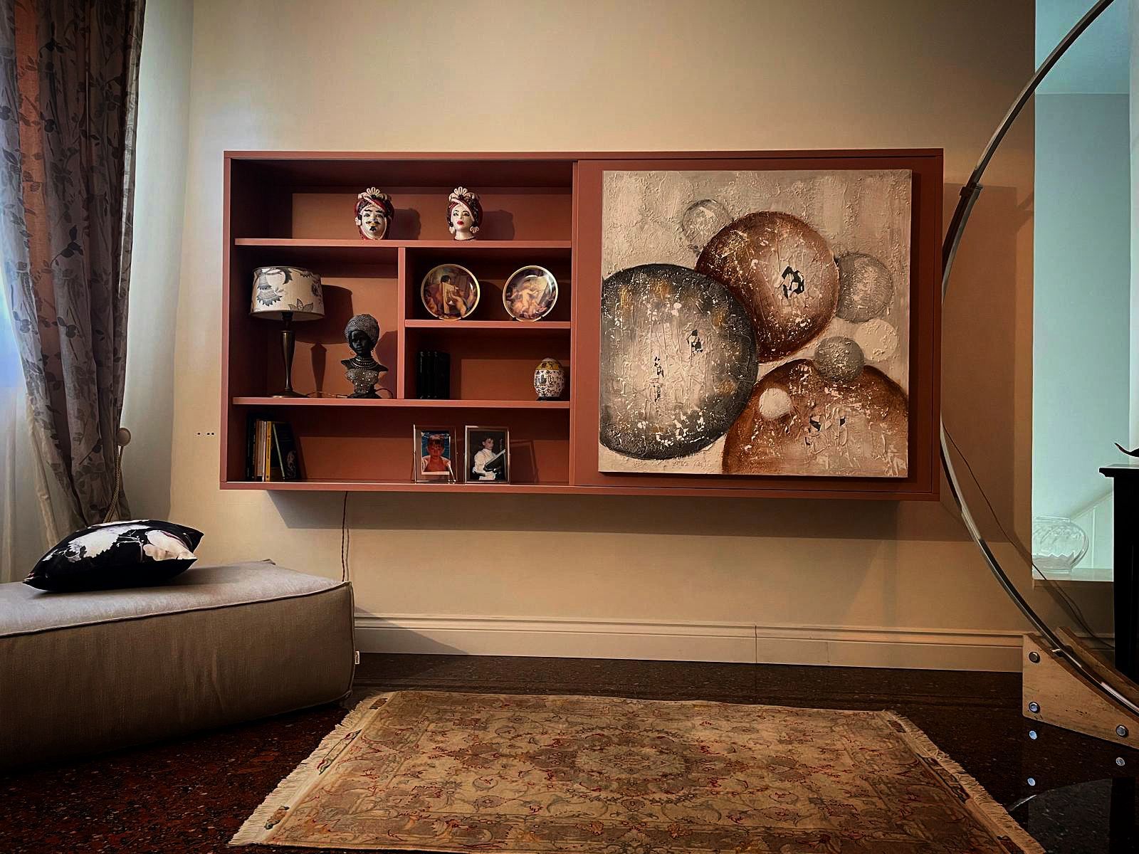 In un soggiorno, una mensola a muro con oggetti decorativi e un quadro astratto a forma di cerchio, posizionata sopra un piccolo divano e un tappeto.