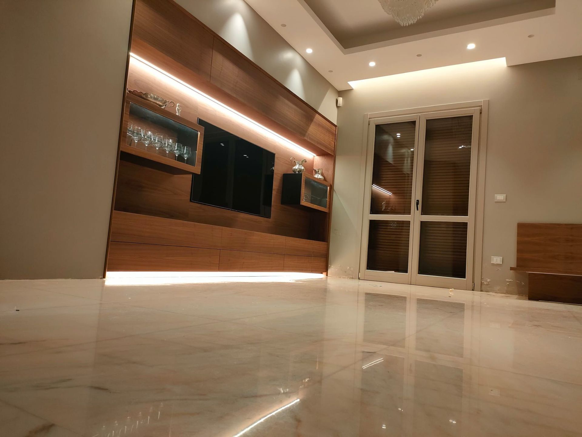 Soggiorno moderno con un elegante mobile TV in legno, illuminazione a incasso e pavimento in marmo lucido.