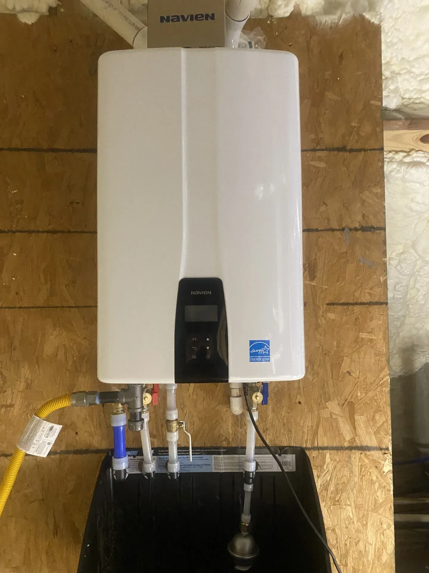 White wall-mounted water heater with pipes and hoses in a utility area