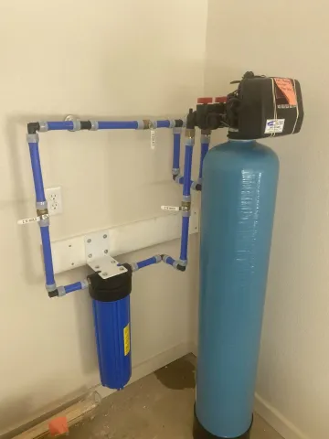 Blue water treatment tank and filter system with pipes mounted against a wall in a utility room