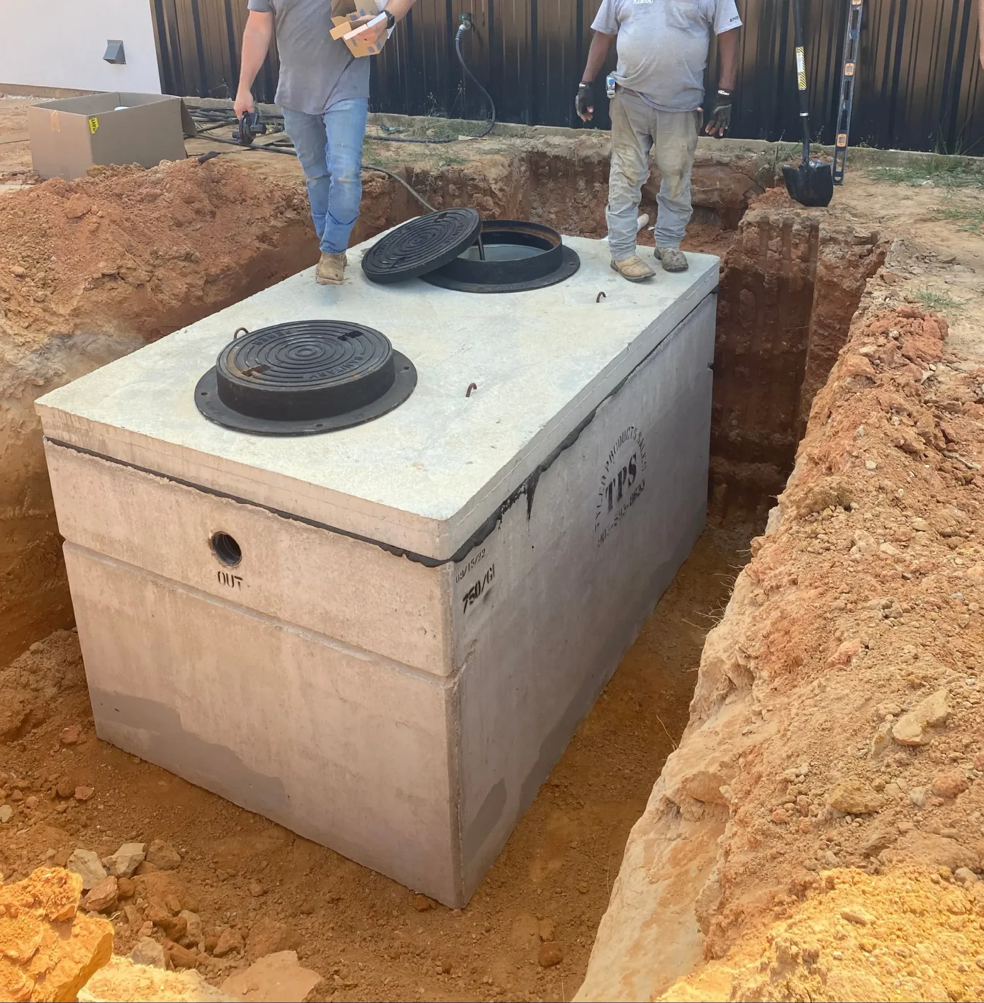 Workers standing beside a large concrete septic tank set in a dug trench at a construction site