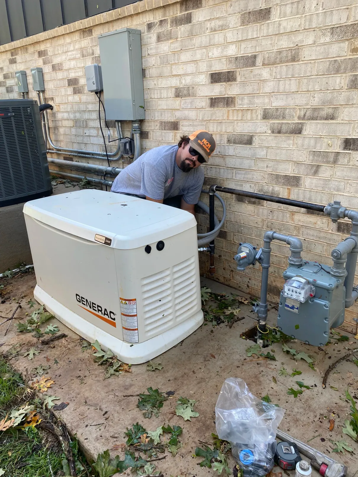Technician working beside a house-mounted generator and gas meter against a brick wall