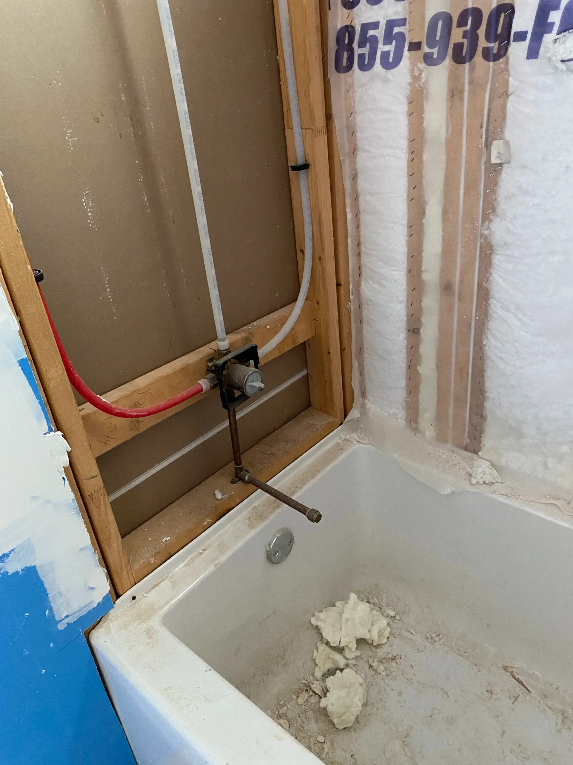 Bathtub with exposed plumbing and unfinished wall repairs around a shower faucet and hose connection