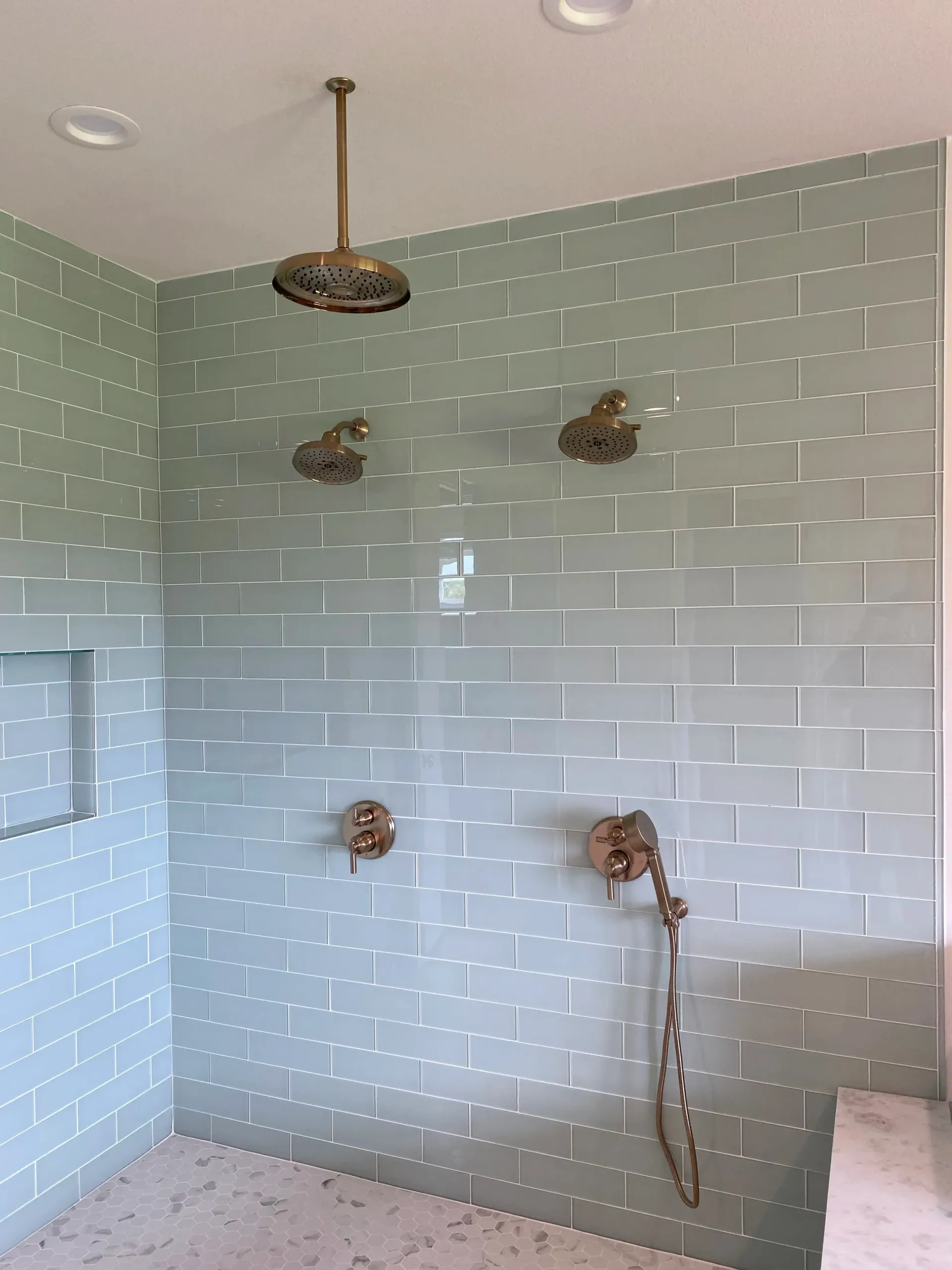 Shower with pale green subway tile, brass fixtures, and handheld showerhead in a bathroom.