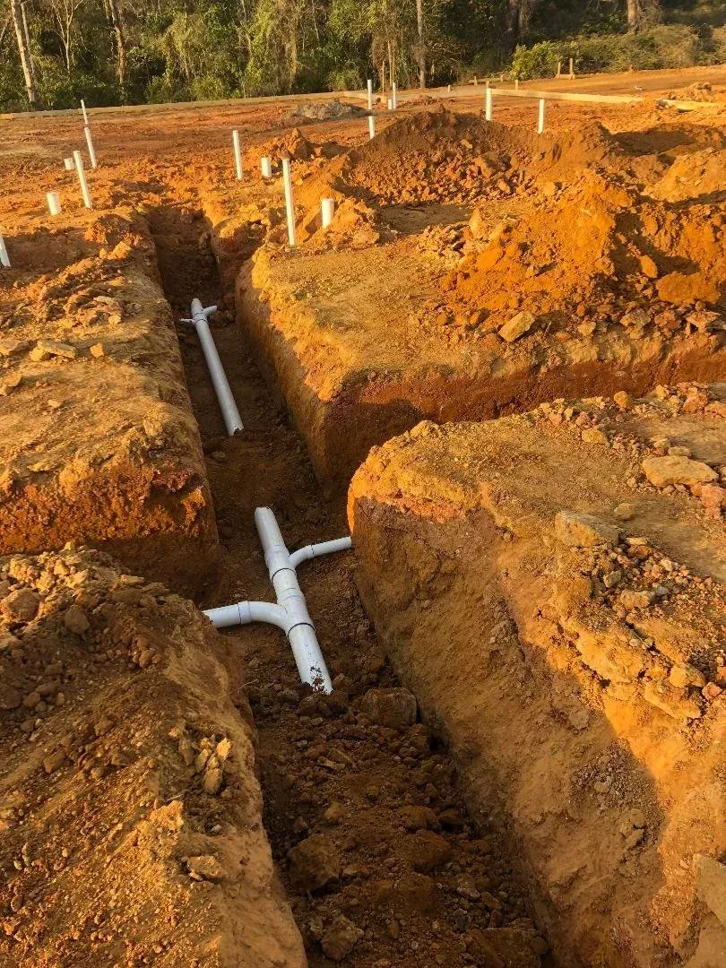 Trenches with white PVC pipes laid in orange-brown soil at a construction site