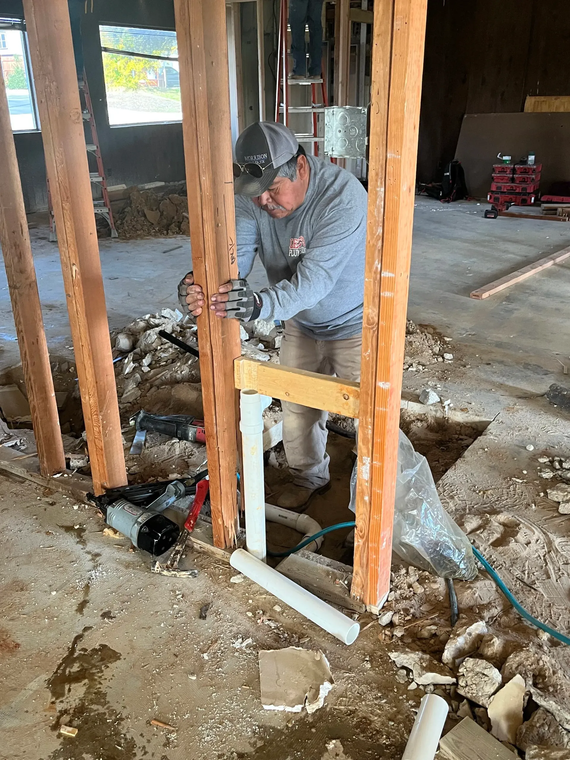 Worker using a tool to cut into a concrete floor inside an unfinished building with exposed studs