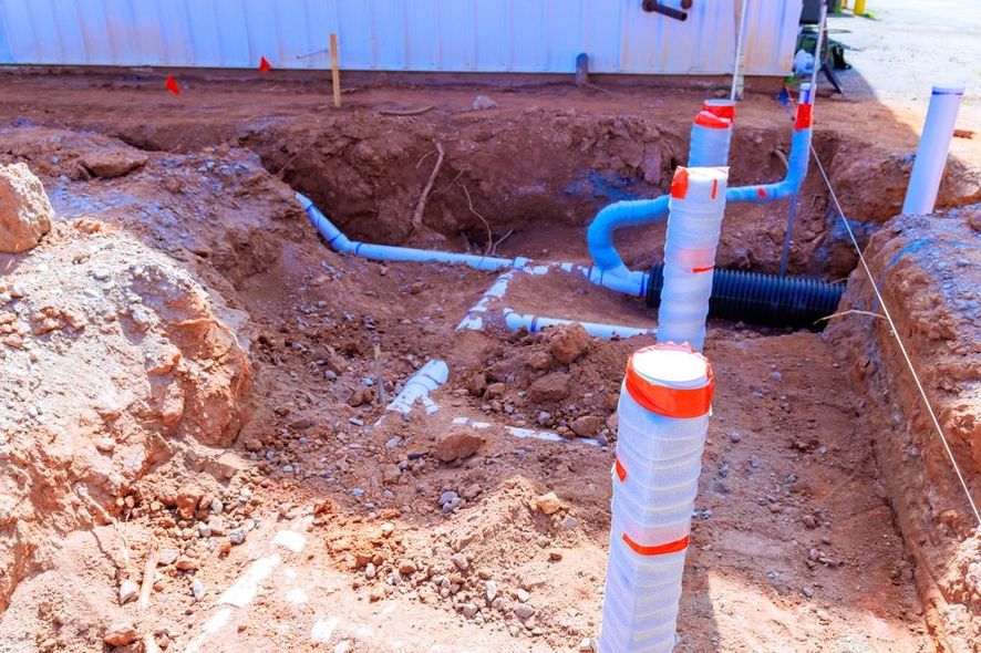Trench with blue underground pipes and orange-capped white posts at a construction site