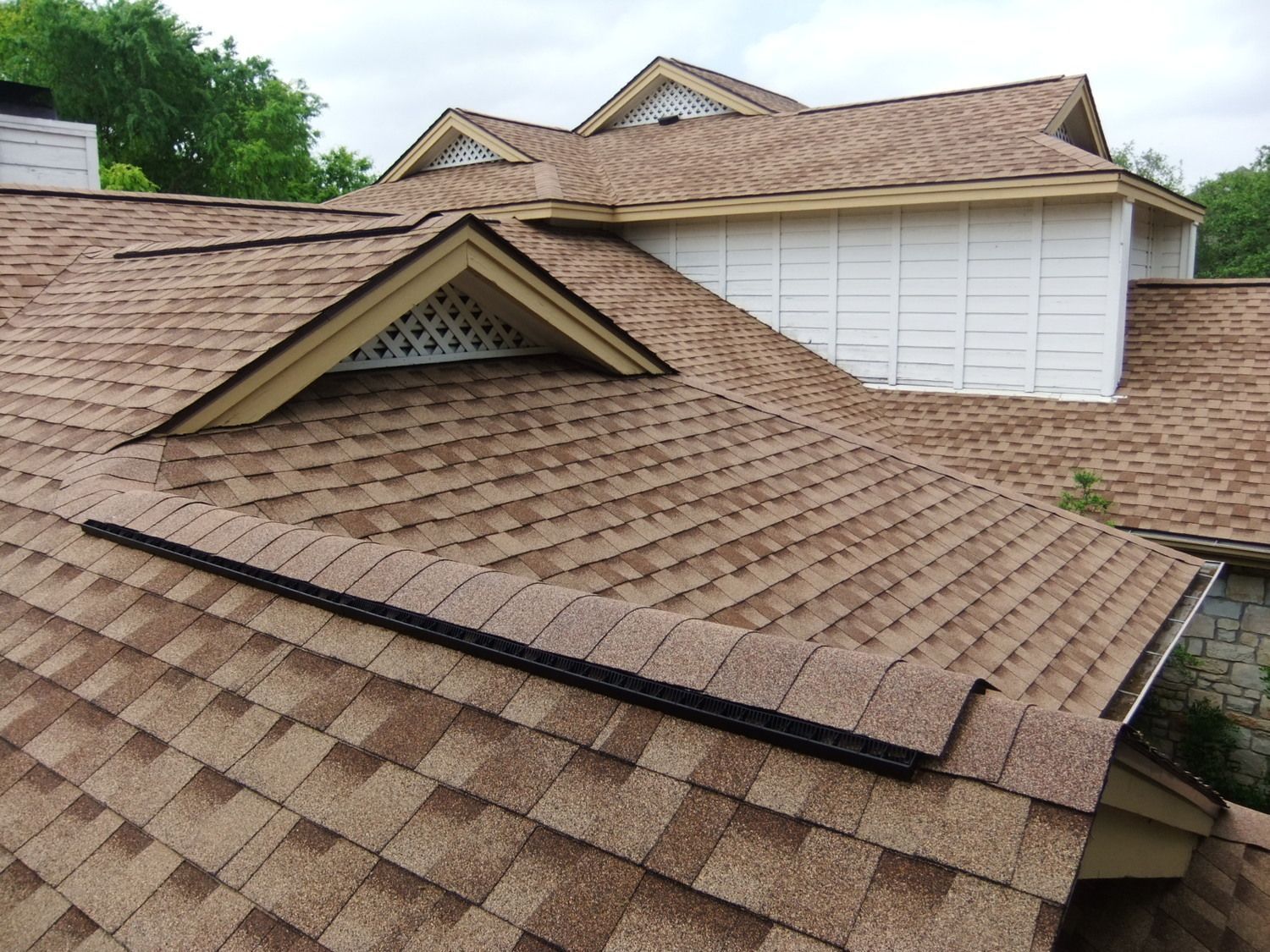 Brown shingle roof with dormer vents and a black ridge vent on a house exterior Brown shingle roof with dormer vents and a black ridge vent on a house exterior