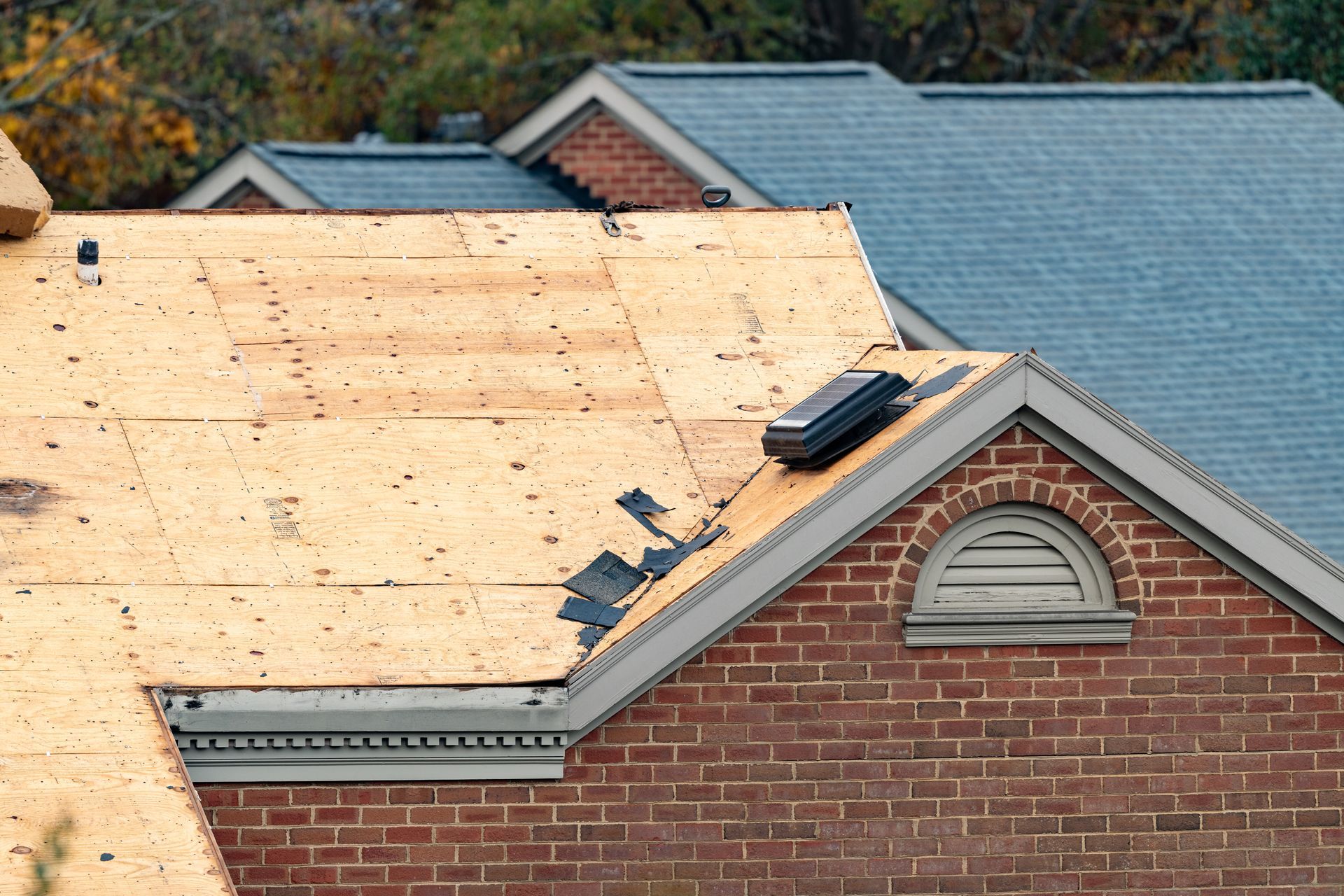 Roof under repair with plywood sheathing, shingles in progress, and two visible skylights on a brick house Roof under repair with plywood sheathing, shingles in progress, and two visible skylights on a brick house