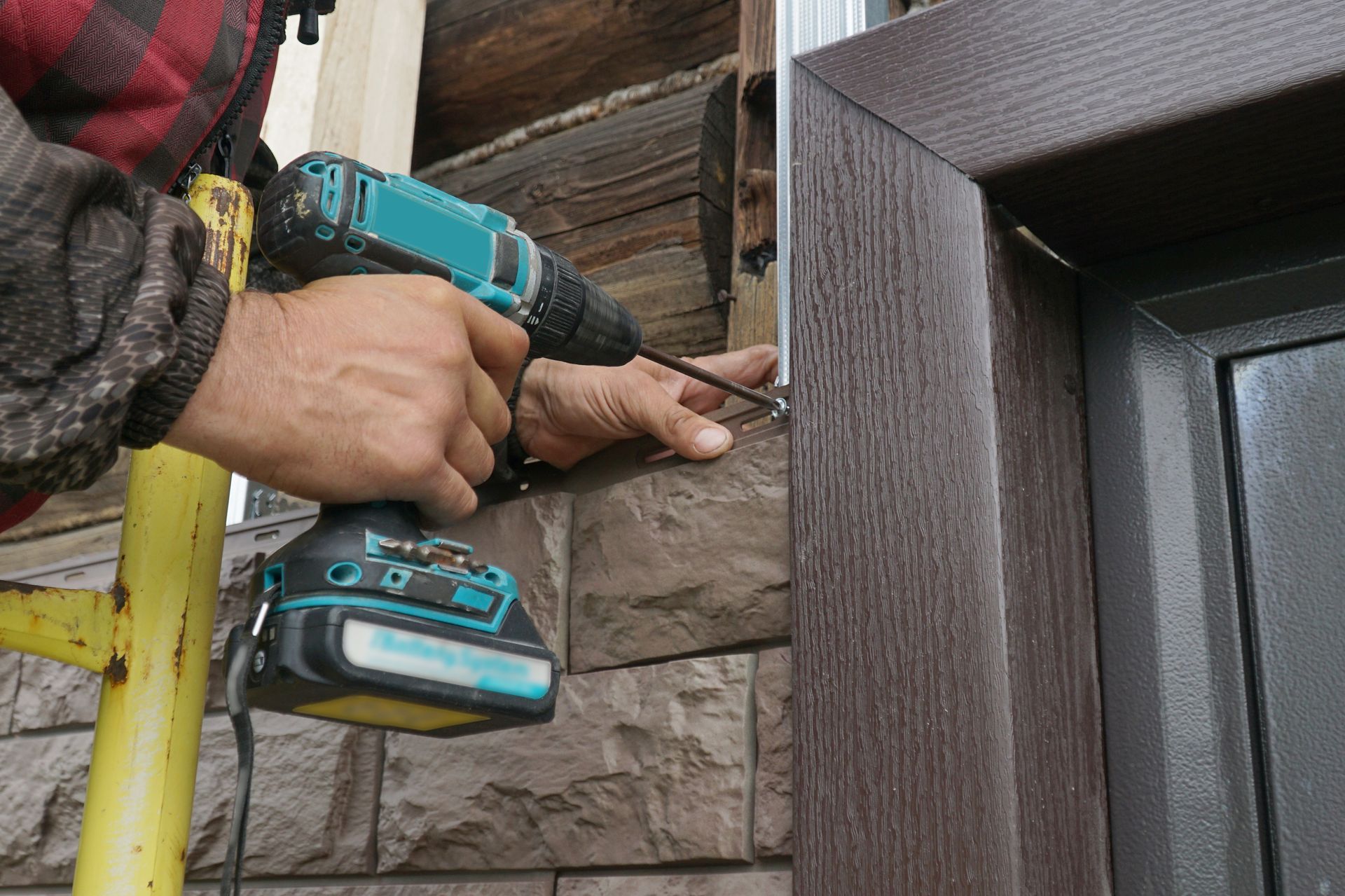 Person using a drill to install trim around a window on an exterior wall