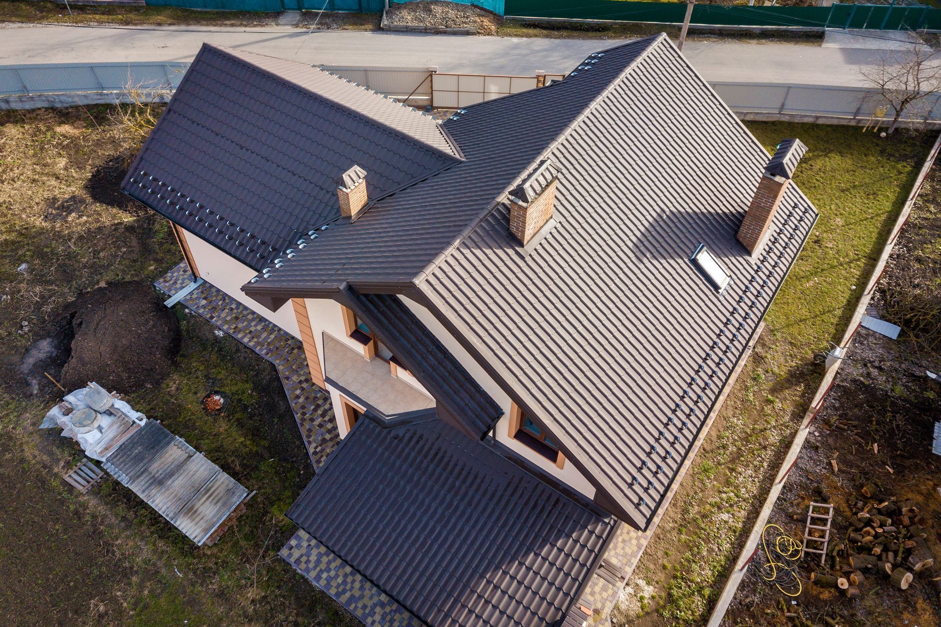 Aerial view of a gray-roofed house with a fenced yard and surrounding construction area Aerial view of a gray-roofed house with a fenced yard and surrounding construction area