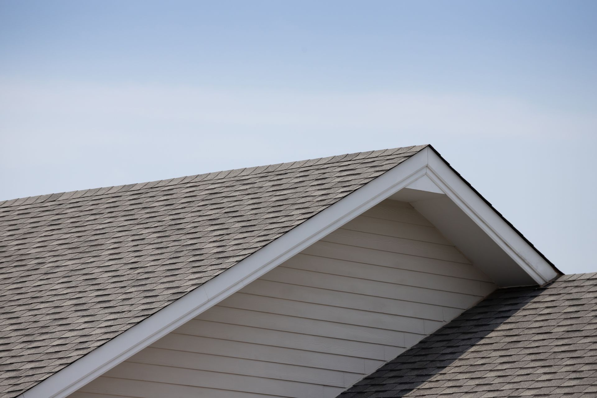 Close-up of a gray shingled roof with a gabled dormer against a blue sky Close-up of a gray shingled roof with a gabled dormer against a blue sky