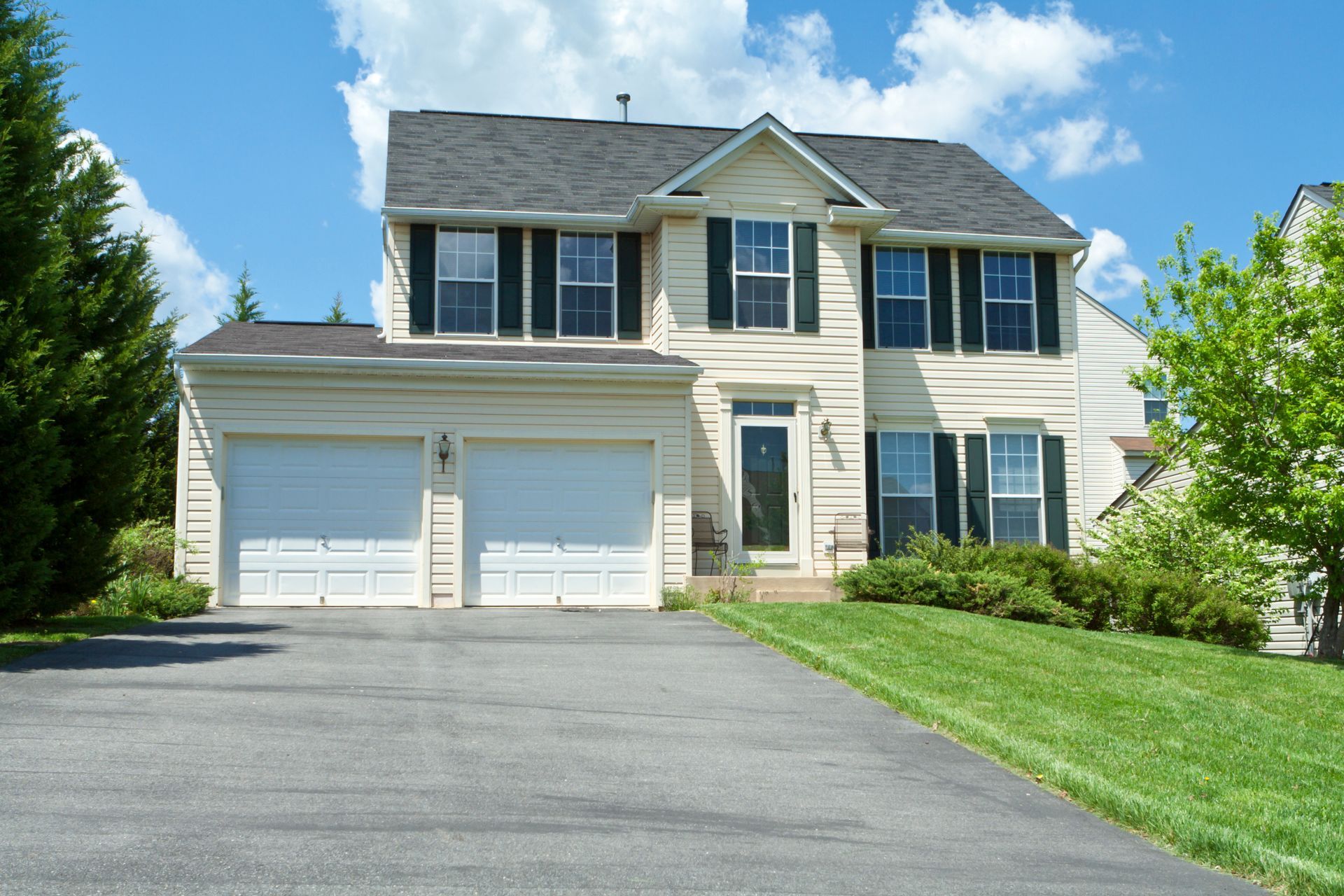 Two-story suburban house with a double garage, driveway, and green lawn under a blue sky