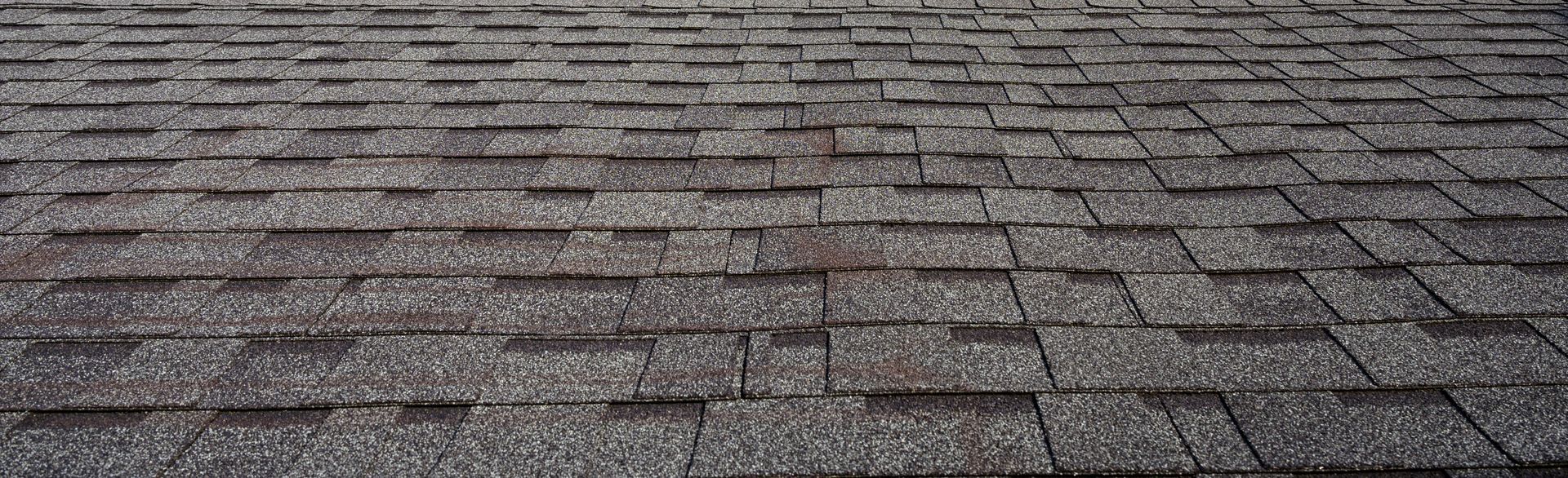 Close-up of gray asphalt shingles on a roof, showing a weathered textured surface.