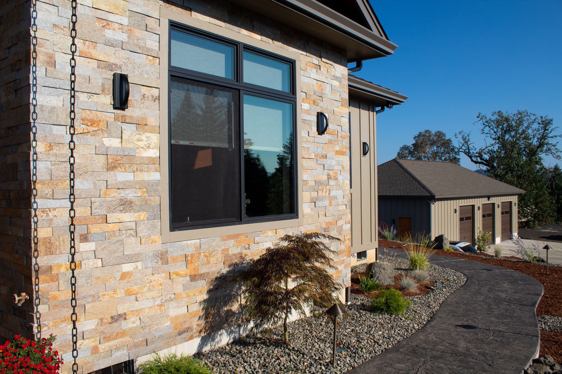 Modern stone house exterior with large windows, landscaped gravel path, and blue sky