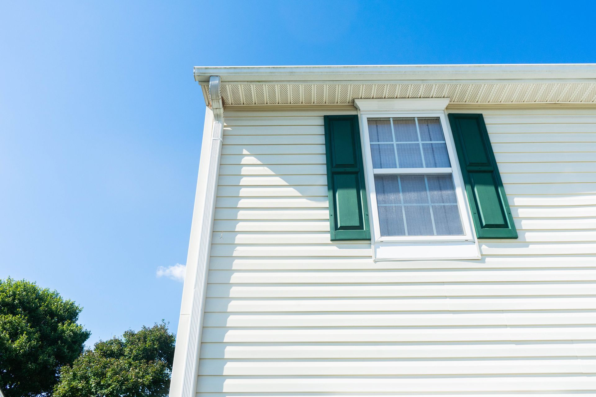 White house siding with green shutters under a clear blue sky White house siding with green shutters under a clear blue sky