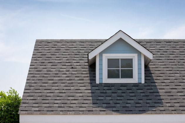 Gray shingled roof with a centered dormer window against a blue sky Gray shingled roof with a centered dormer window against a blue sky
