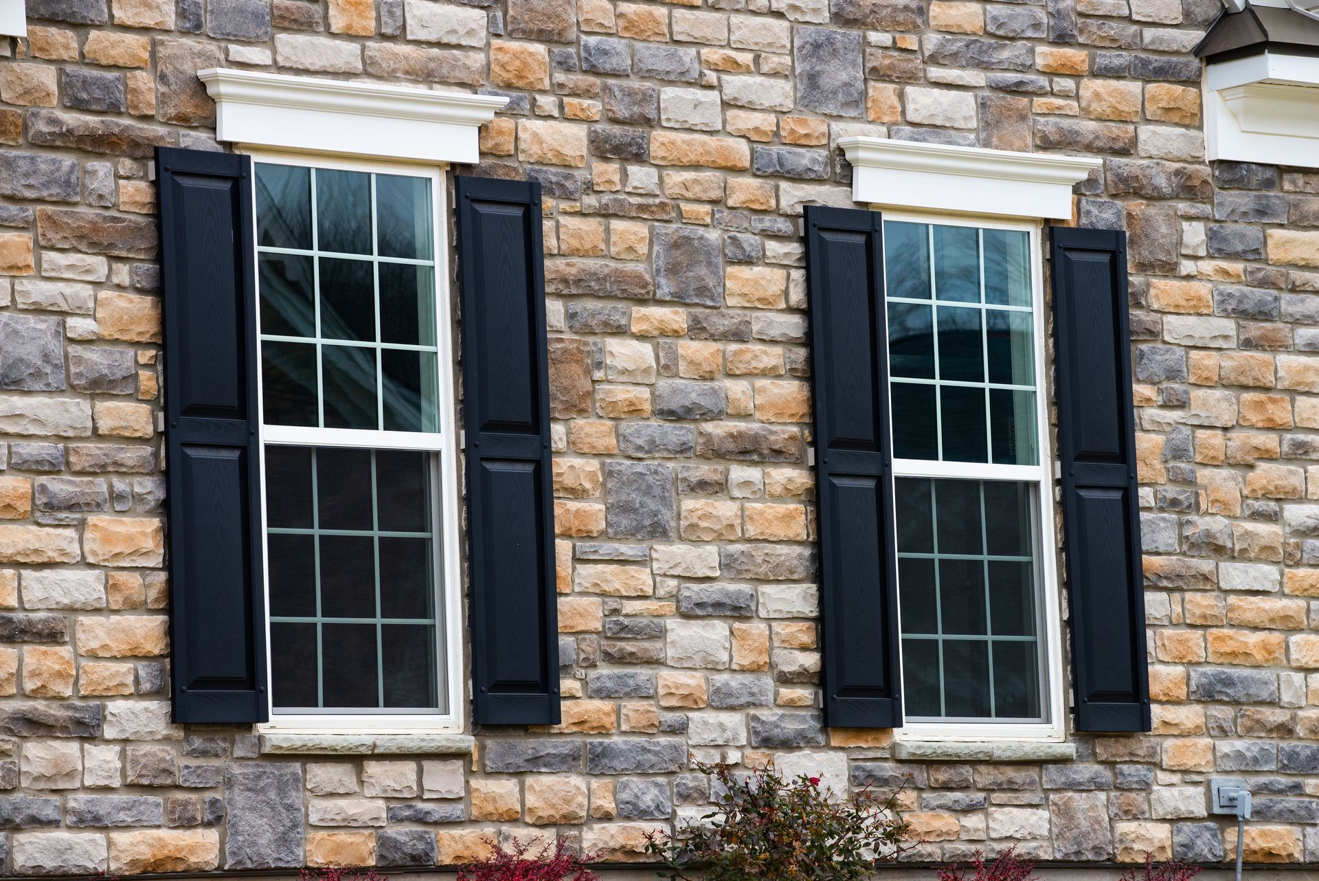 Stone building facade with two white-paned windows and dark shutters