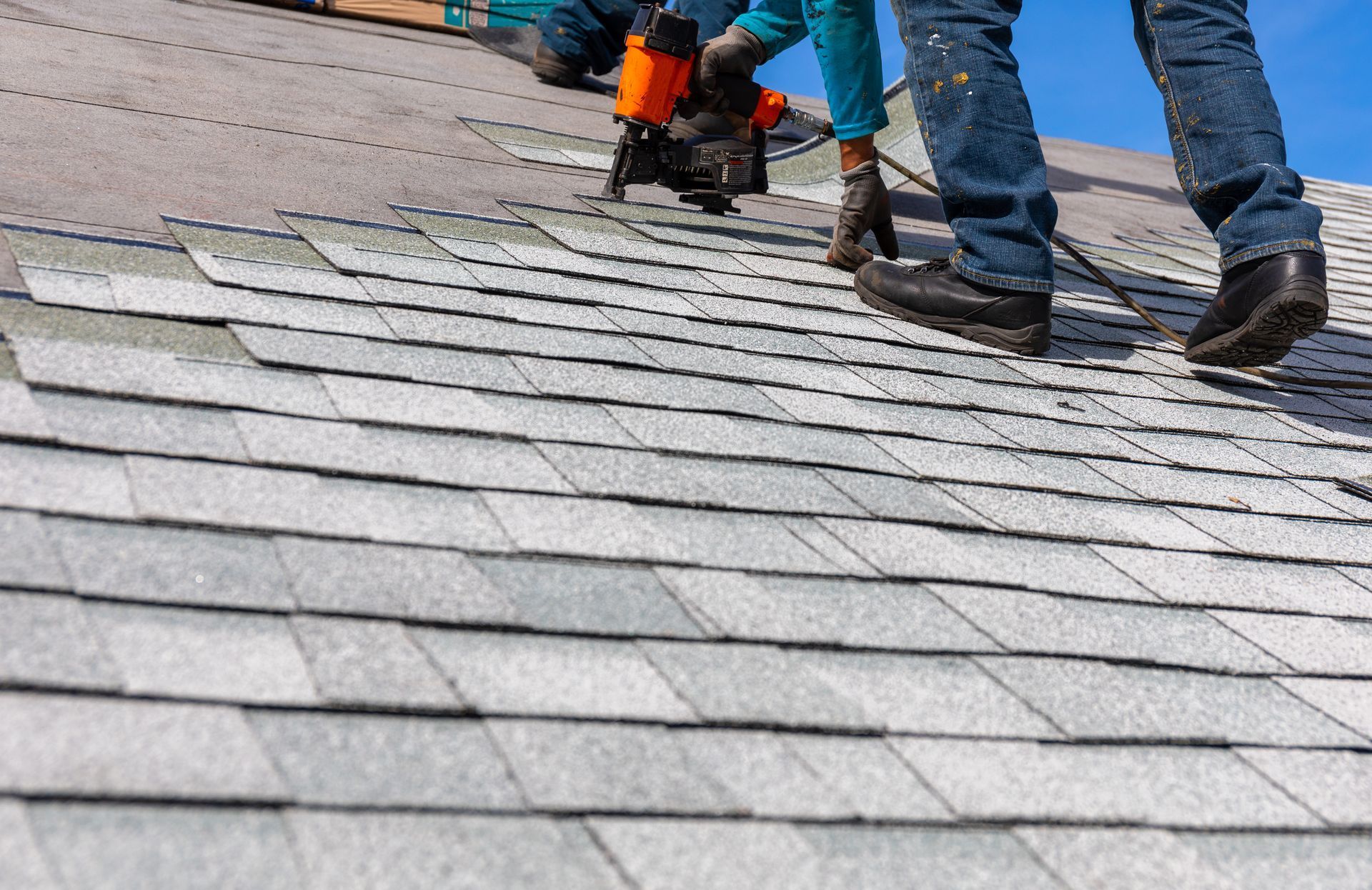 Workers repairing a gray shingled roof with tools on a sloped rooftop
